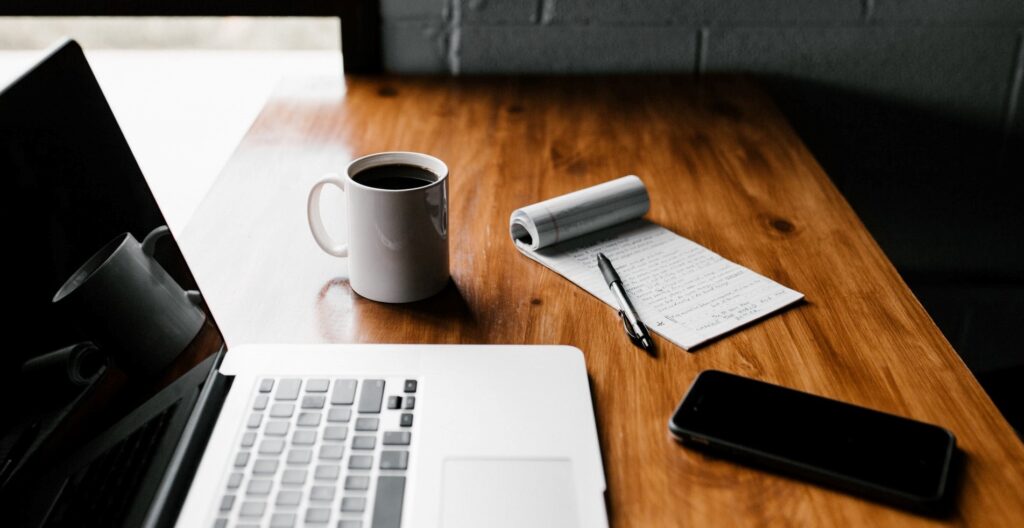 Laptop Computer next to Writing Pad, Ballpoint Pen, and Black Coffee